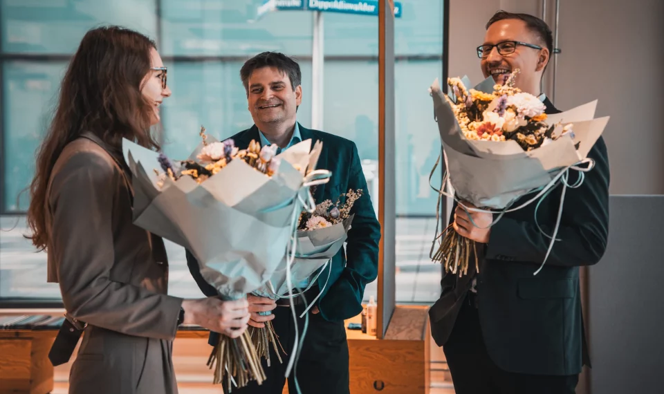 Teammitglieder von public.consulting mit Blumensträußen bei einer Ehrung im Büro