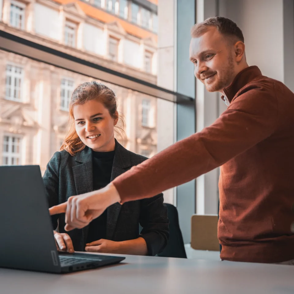 Zwei Teammitglieder von public.consulting besprechen Inhalte auf einem Laptop am Fenster